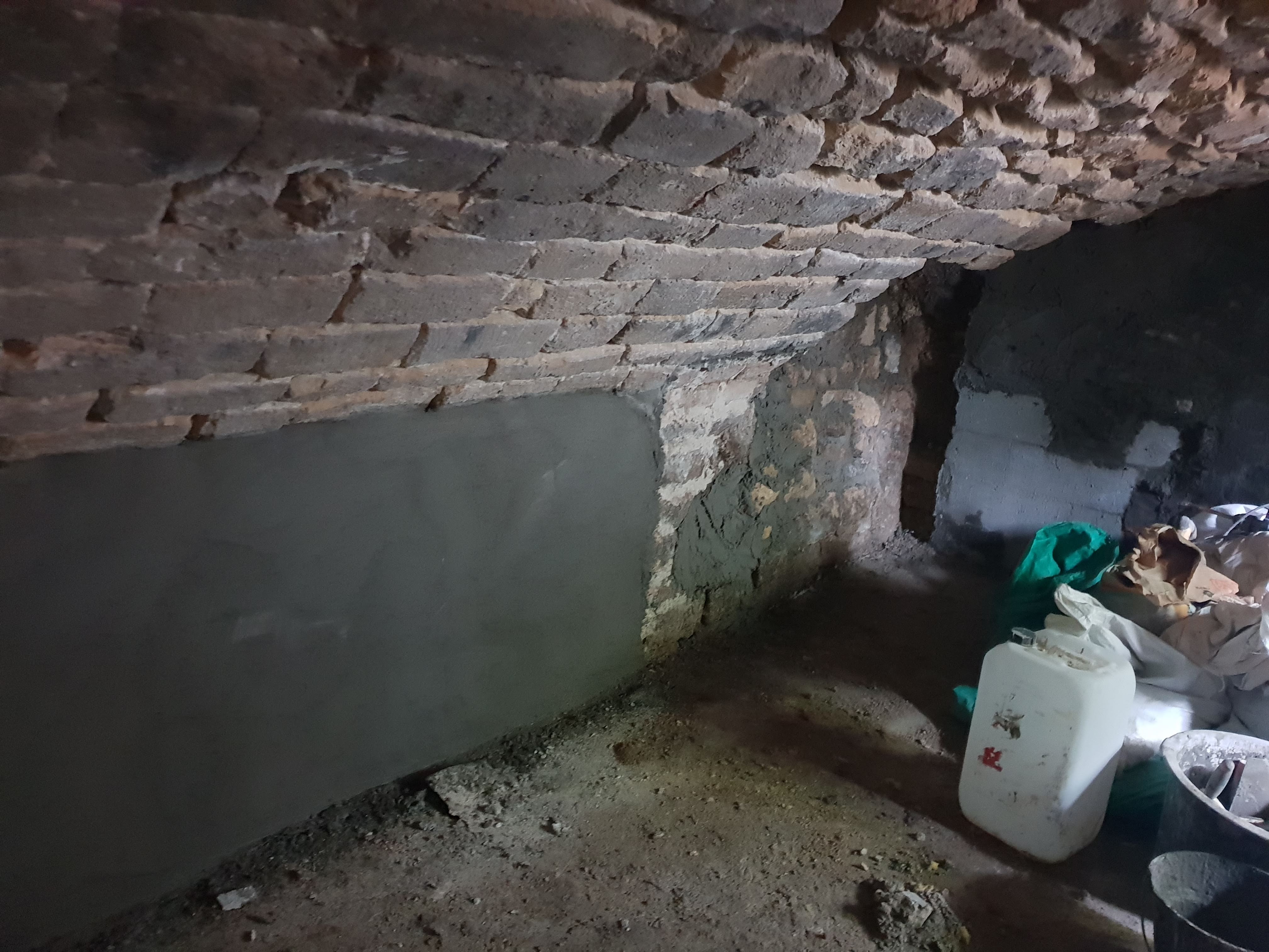 Cave voûtée en pierre humide, cuvelage du bas des murs en cours pour traiter la nappe et les infiltrations