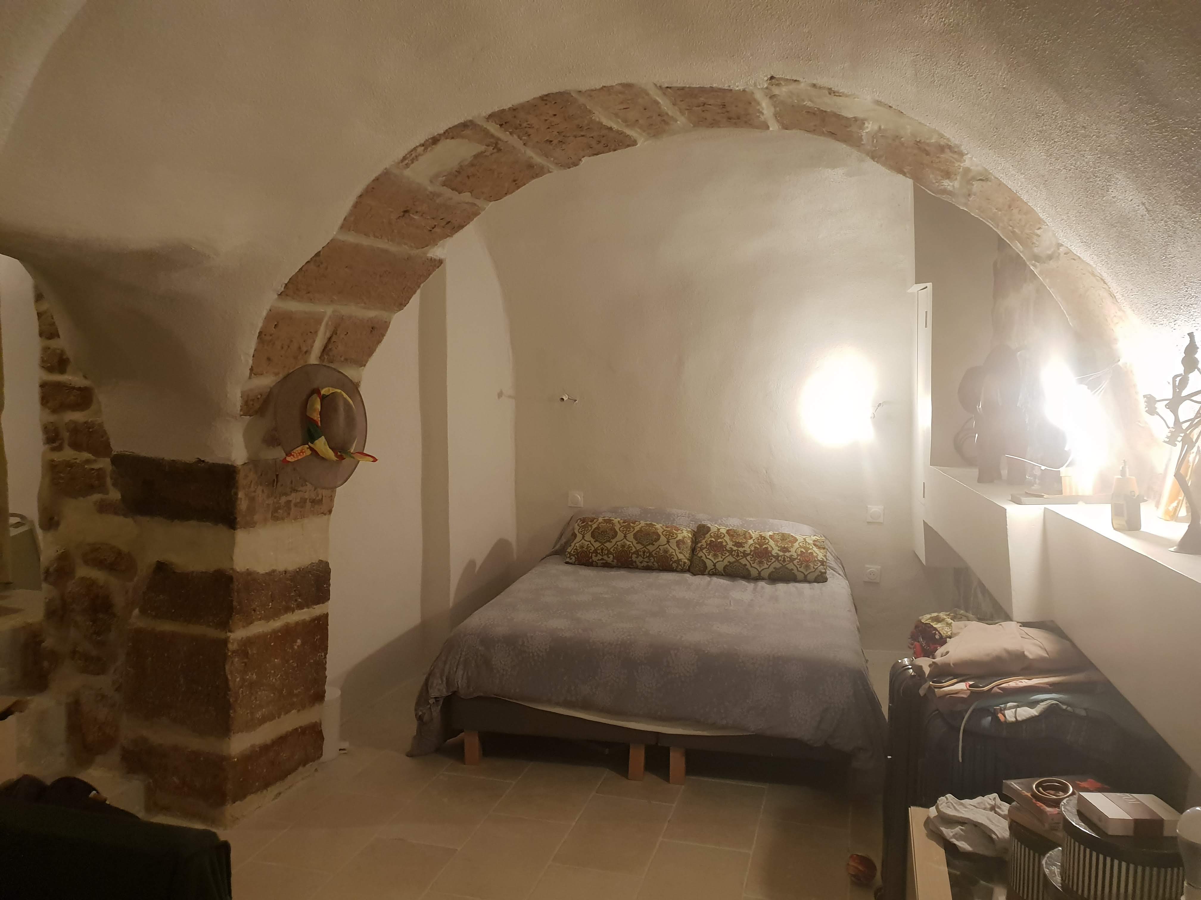 Cave transformée en chambre à coucher : voûte et arche en pierre apparente, lit, éclairage chaleureux