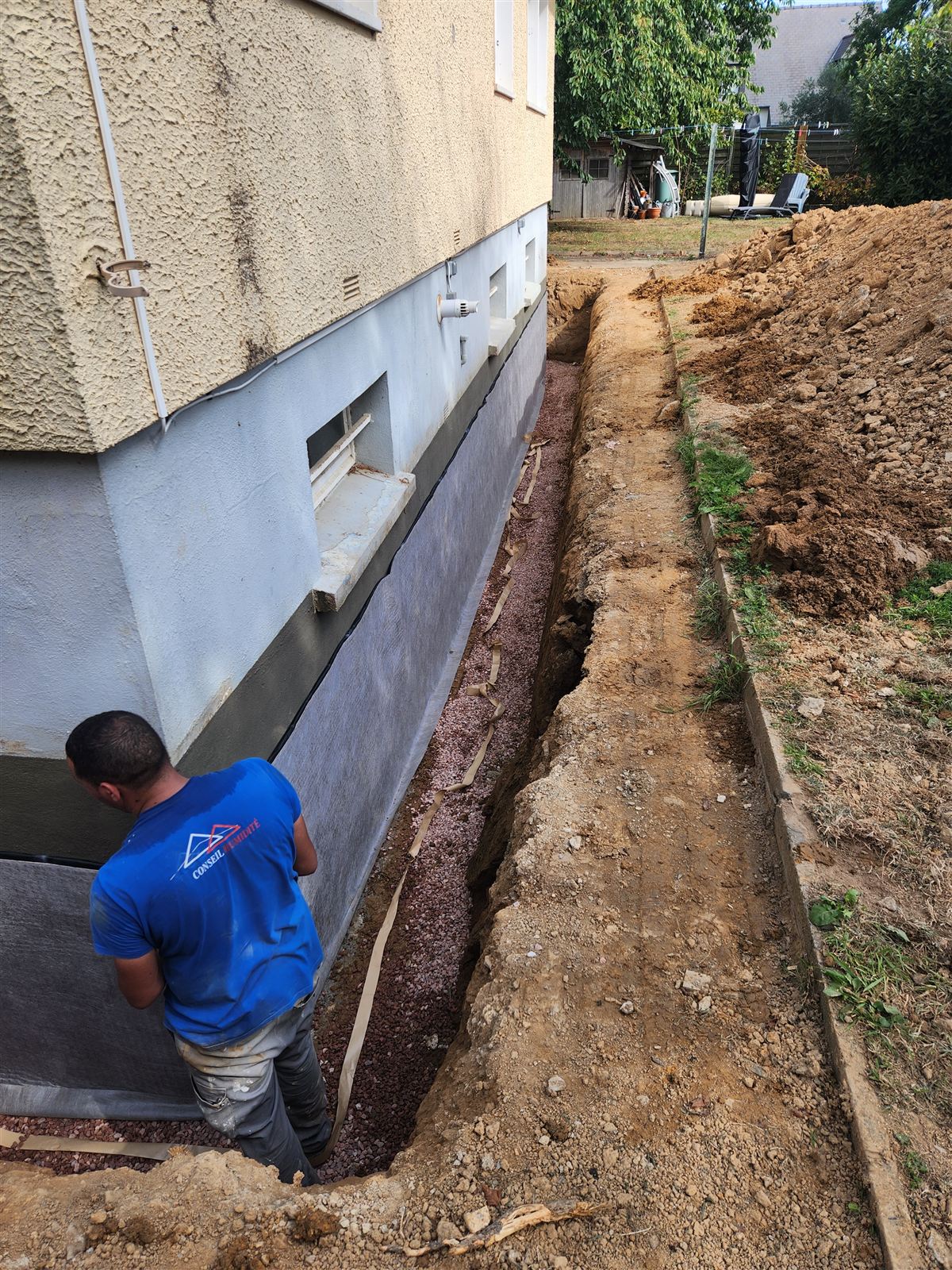 Technicien France Conseil Humidité posant l'étanchéité et le drainage le long d'une fondation