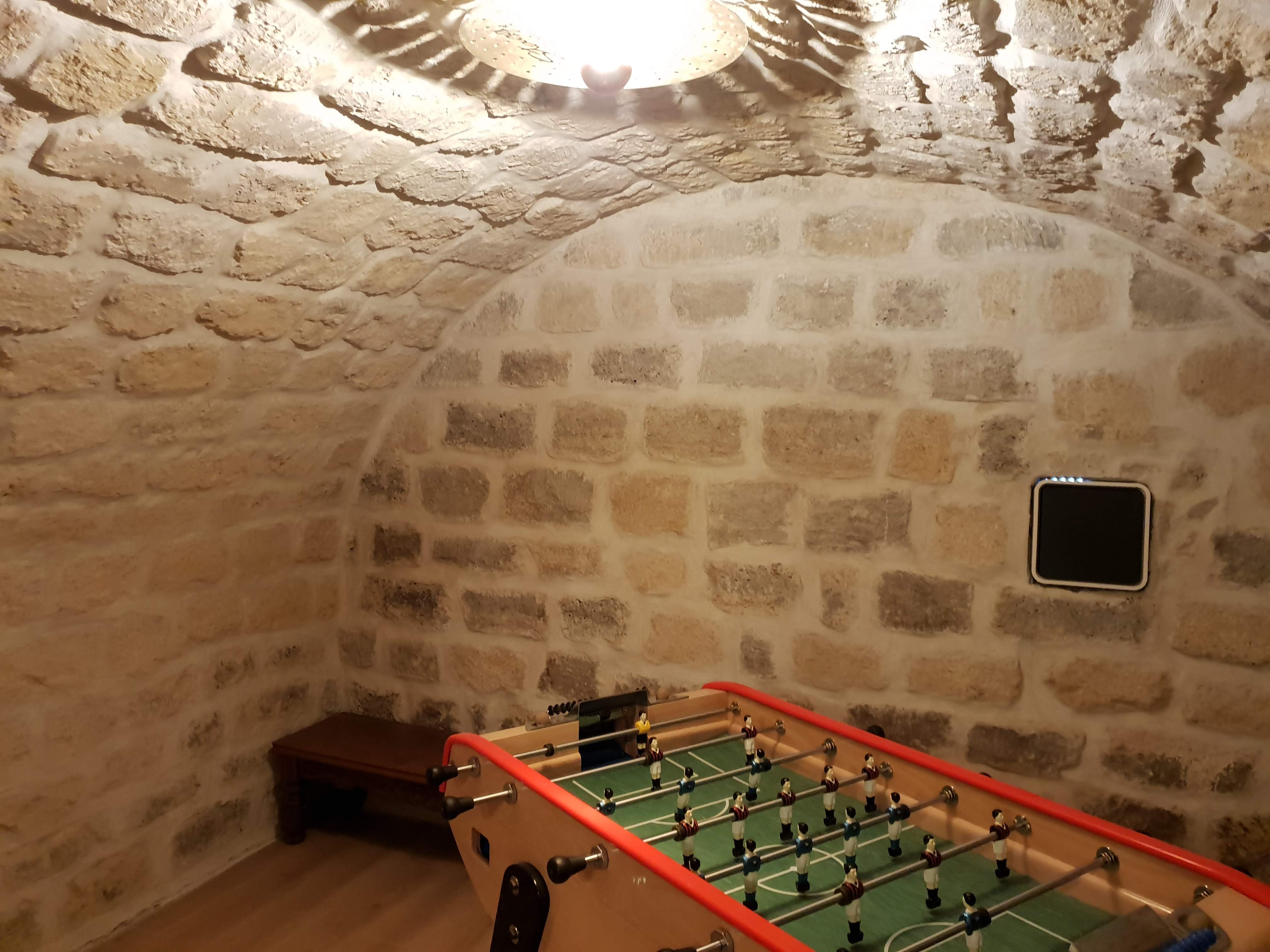 Cave voûtée aux Lilas aménagée en salle de jeux avec baby-foot sous la voûte en pierre rejointoyée