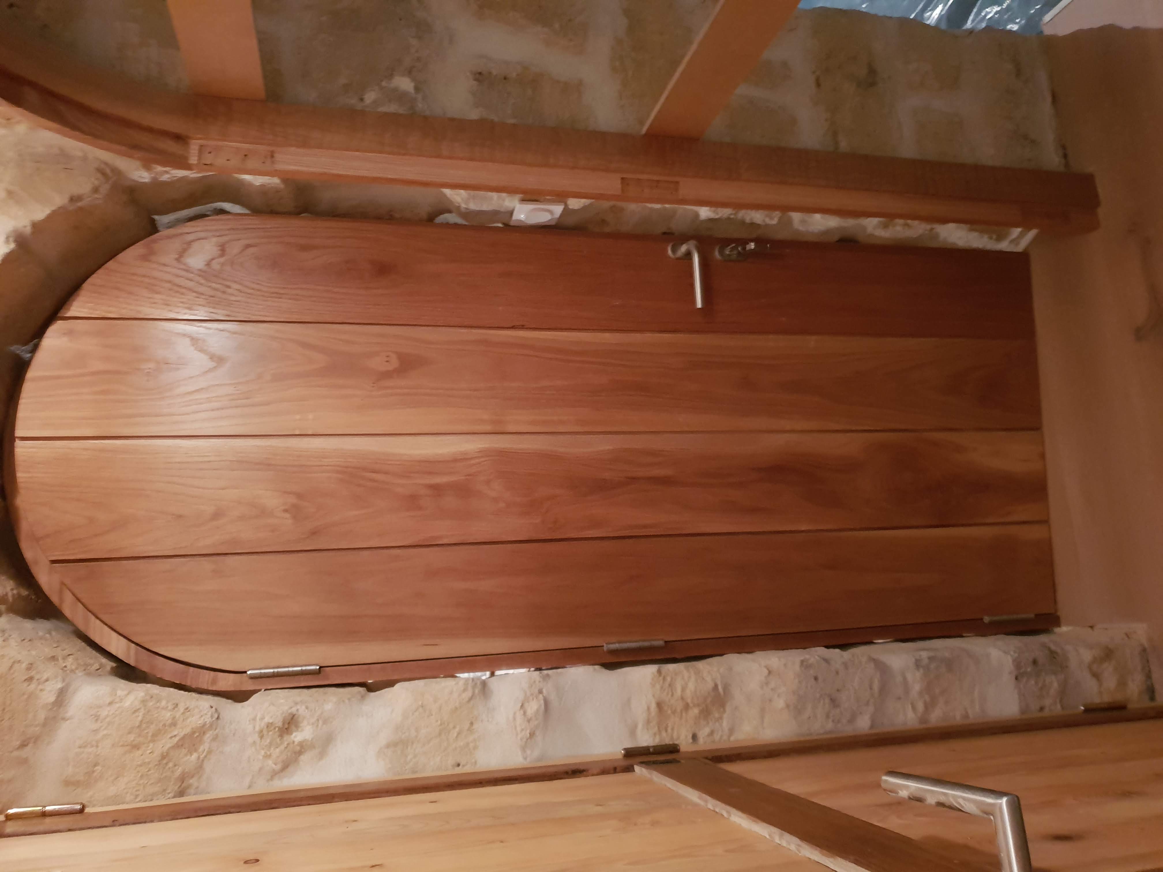 Porte cintrée en bois sur mesure installée dans l'arche en pierre de la cave aux Lilas